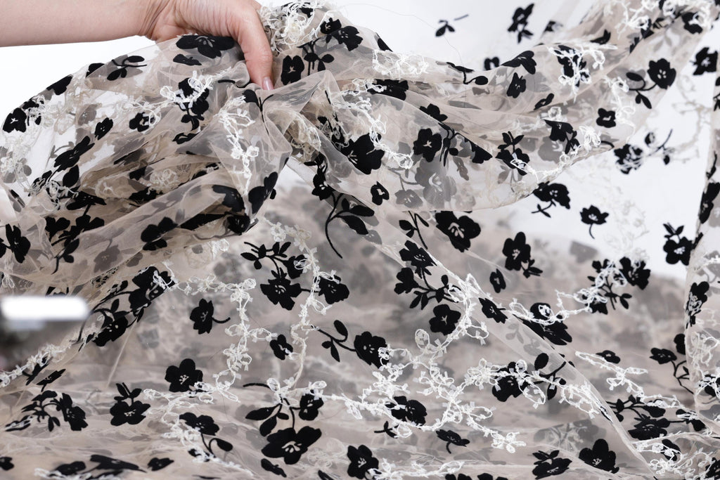 A hand is holding up a piece of fabric with a black and white floral pattern.