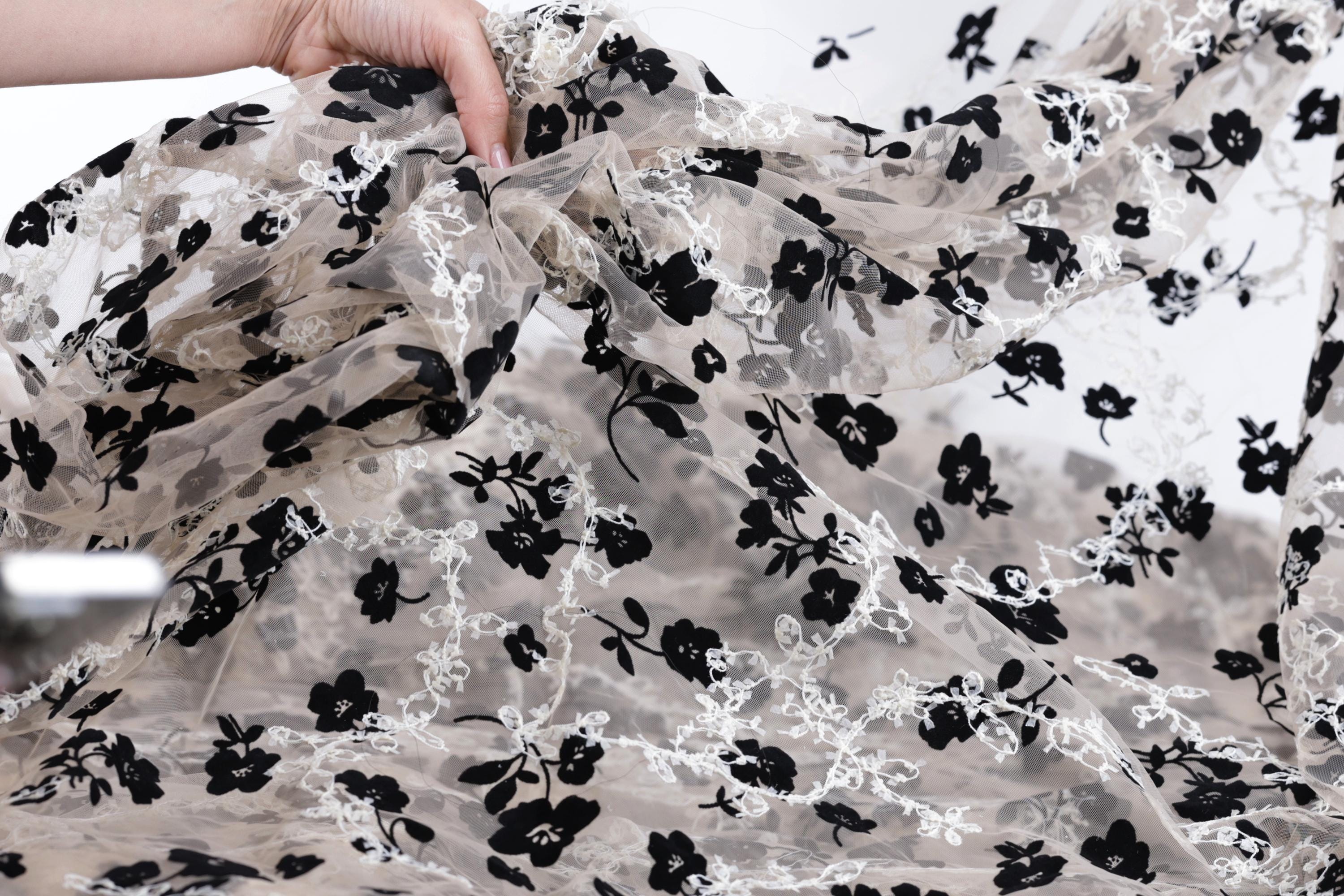 A hand is holding up a piece of fabric with a black and white floral pattern.