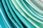 a close-up view of a collection of turquoise-colored fabric, showcasing the fabric's smooth and shiny texture.