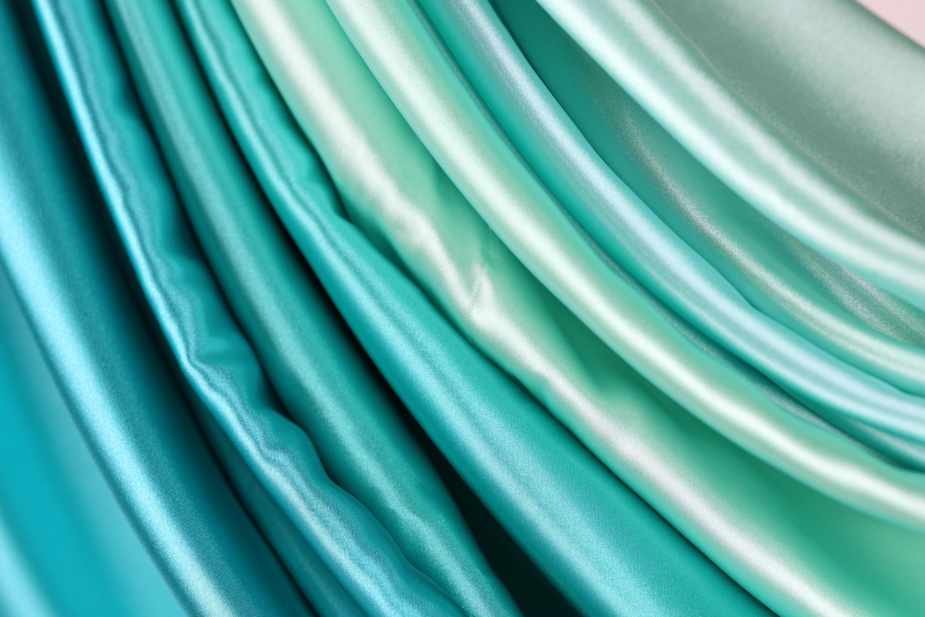 a close-up view of a collection of turquoise-colored fabric, showcasing the fabric's smooth and shiny texture.