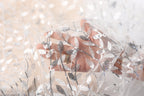 A hand is holding a piece of white fabric with a silver leaf pattern, partially obscured by the fabric.