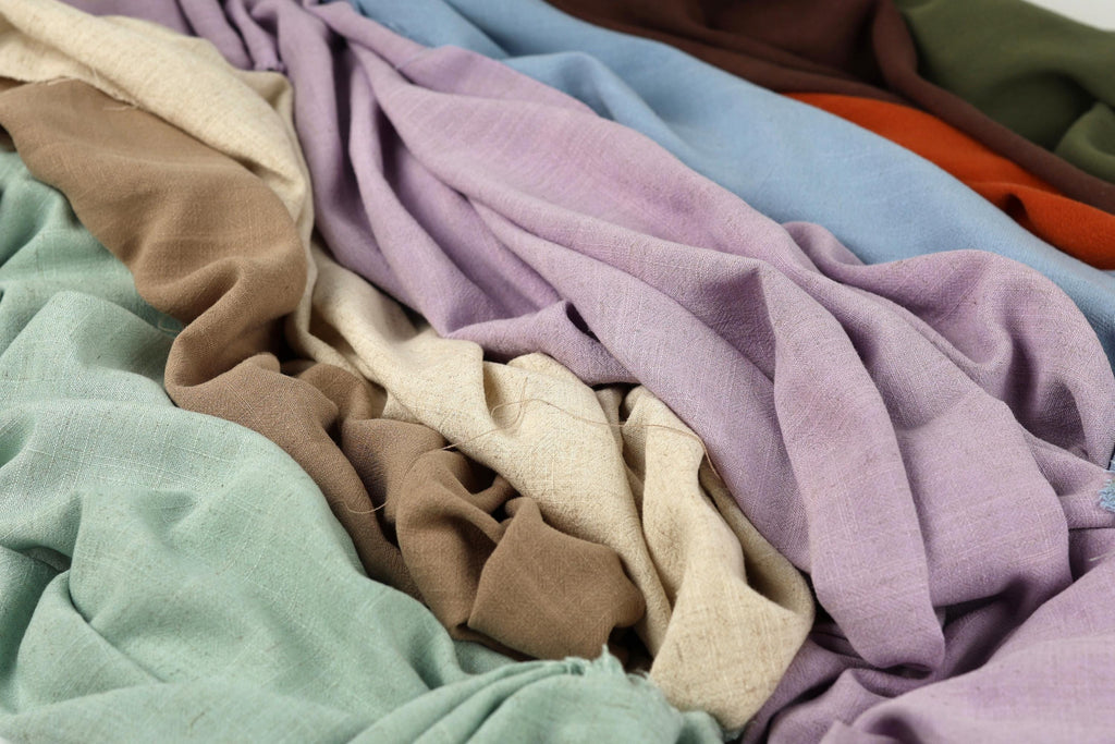 a close-up view of various colorful fabrics, including shades of purple, green, and brown, arranged in a crumpled and messy manner.