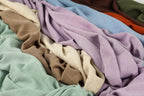 a close-up view of various colorful fabrics, including shades of purple, green, and brown, arranged in a crumpled and messy manner.