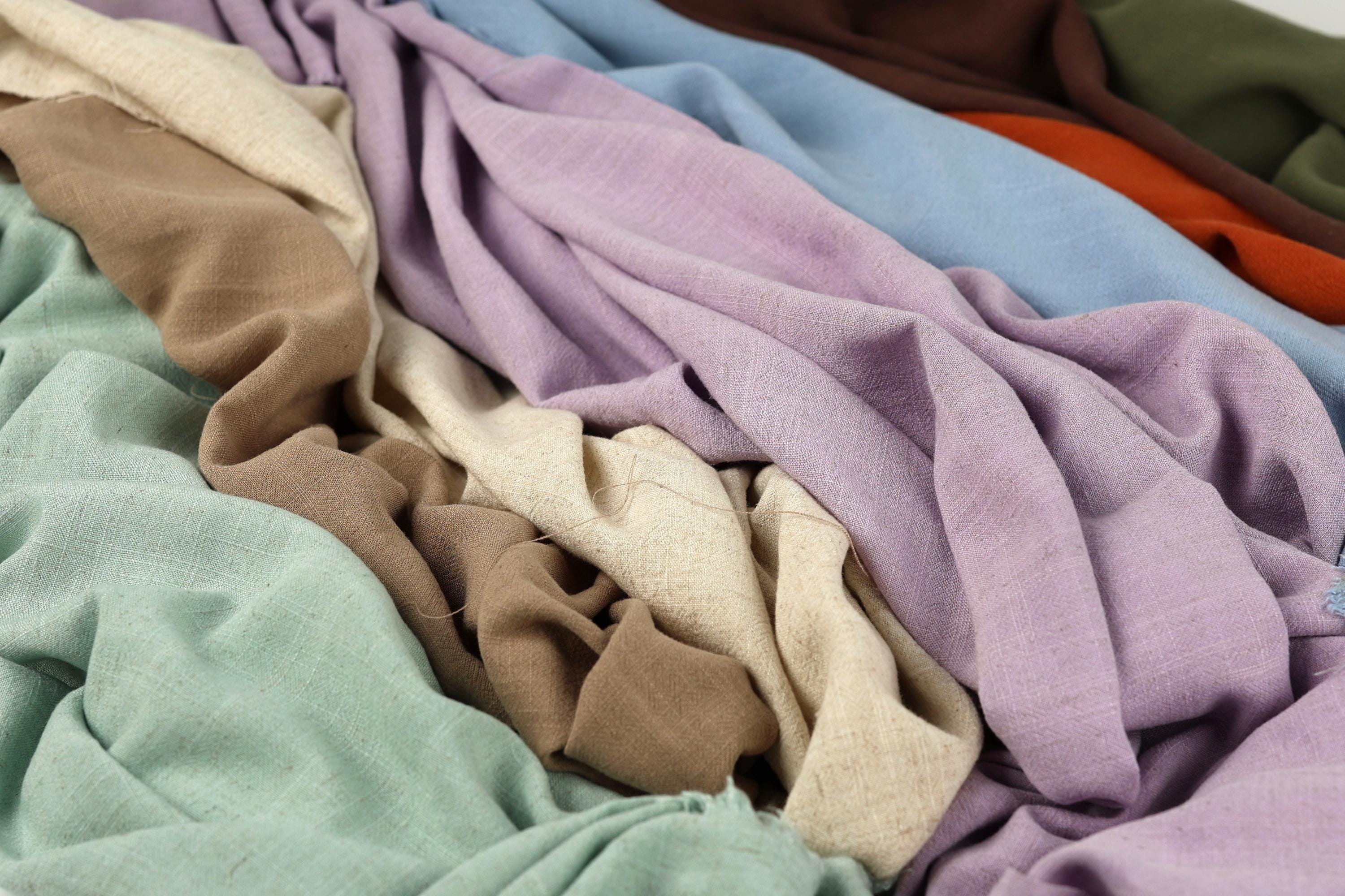 a close-up view of various colorful fabrics, including shades of purple, green, and brown, arranged in a crumpled and messy manner.