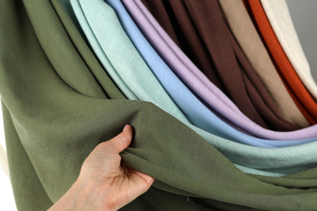 A hand is holding a green fabric, possibly a piece of clothing or a textile, and is examining it closely.