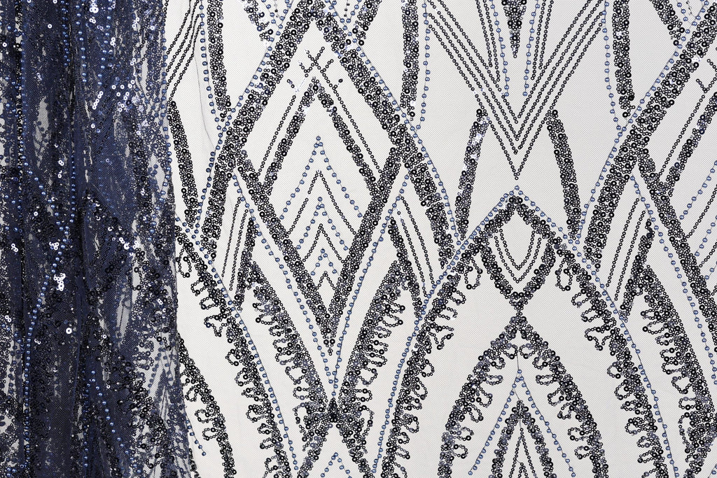 a close-up view of a fabric with a repeating pattern of black and white diamond shapes, interspersed with small blue sequins. The pattern is intricate and visually striking, with the contrasting colors and shapes creating a sense of depth and texture.