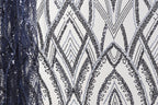 a close-up view of a fabric with a repeating pattern of black and white diamond shapes, interspersed with small blue sequins. The pattern is intricate and visually striking, with the contrasting colors and shapes creating a sense of depth and texture.