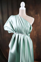 A mannequin wearing a one-shoulder, draped green dress with a pleated design.