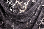 The image is a close-up view of a black and white fabric with a floral pattern. The fabric appears to be made of lace or a similar material, with a mix of black and white colors. The fabric has a textured and intricate appearance, with visible threads or strands running through the fabric.