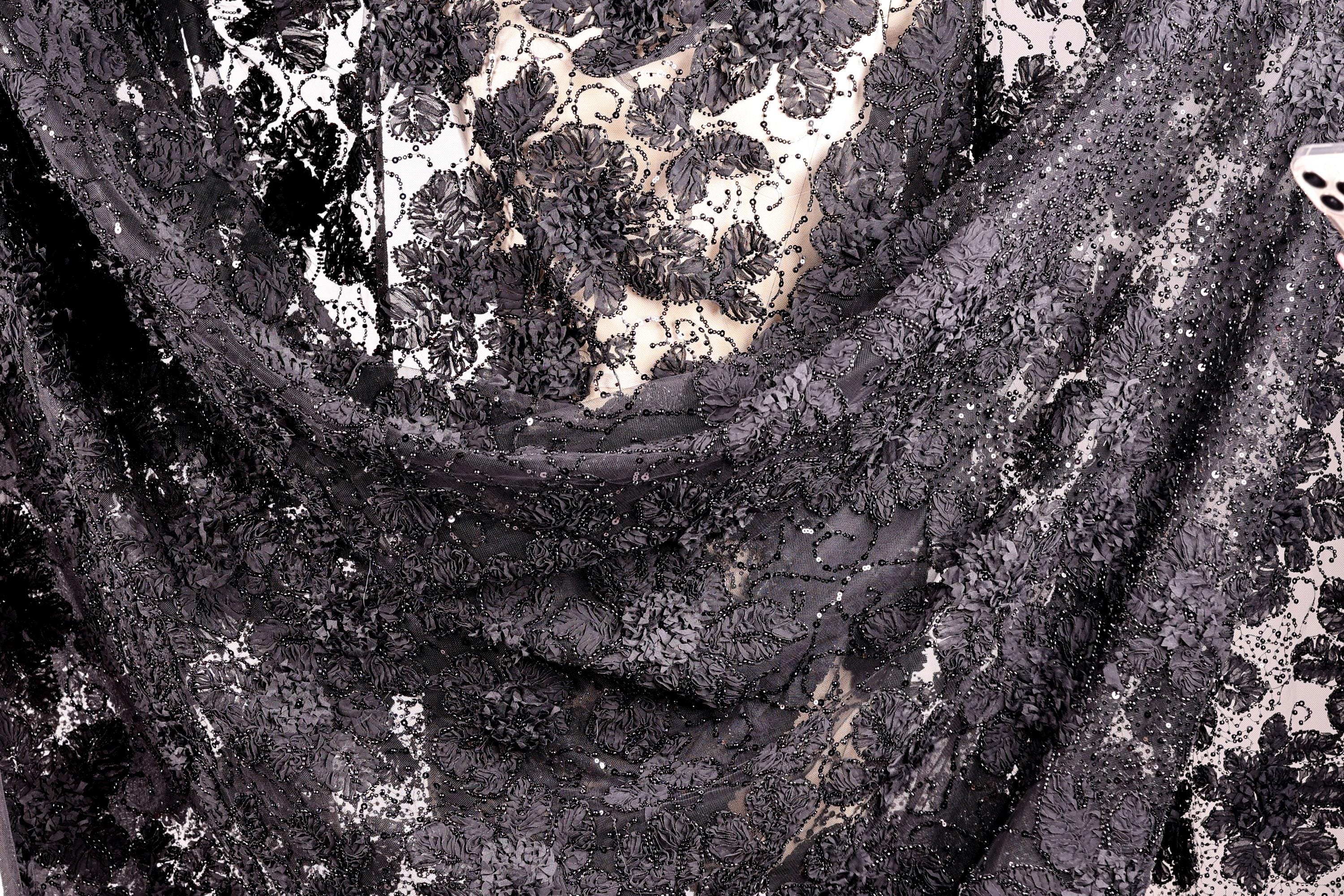 The image is a close-up view of a black and white fabric with a floral pattern. The fabric appears to be made of lace or a similar material, with a mix of black and white colors. The fabric has a textured and intricate appearance, with visible threads or strands running through the fabric.