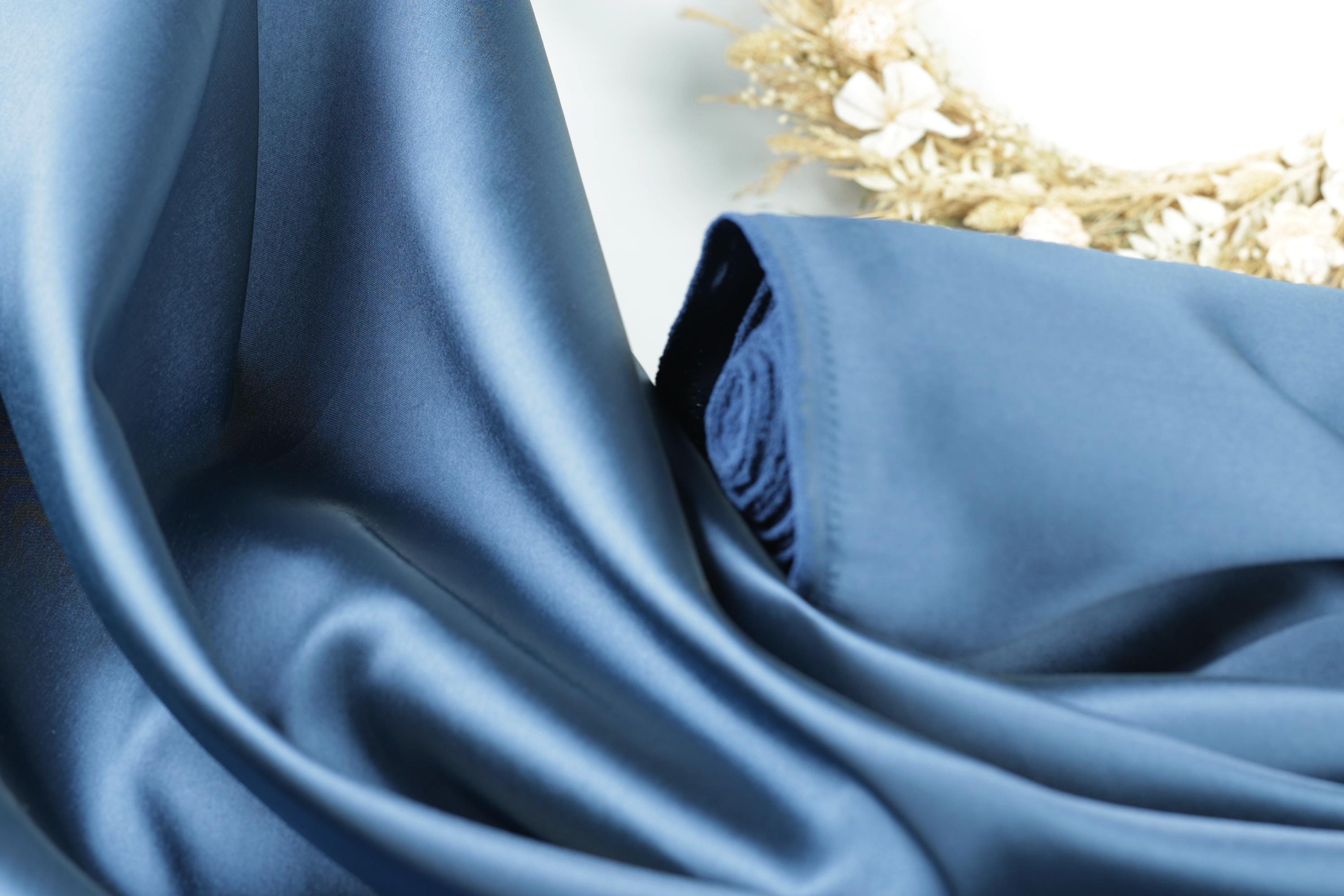 a close-up view of a blue satin fabric, with a wreath of dried flowers in the background.