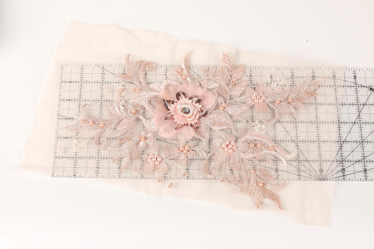 a delicate floral embroidery with a pink flower and leaves, placed on a transparent ruler.