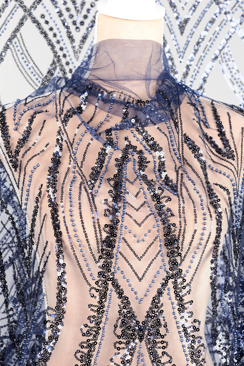 a mannequin wearing a dress with a sheer, sequined bodice. The dress has a pattern of blue and black sequins, creating a visually striking and intricate design.
