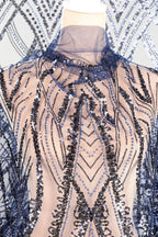 a mannequin wearing a dress with a sheer, sequined bodice. The dress has a pattern of blue and black sequins, creating a visually striking and intricate design.