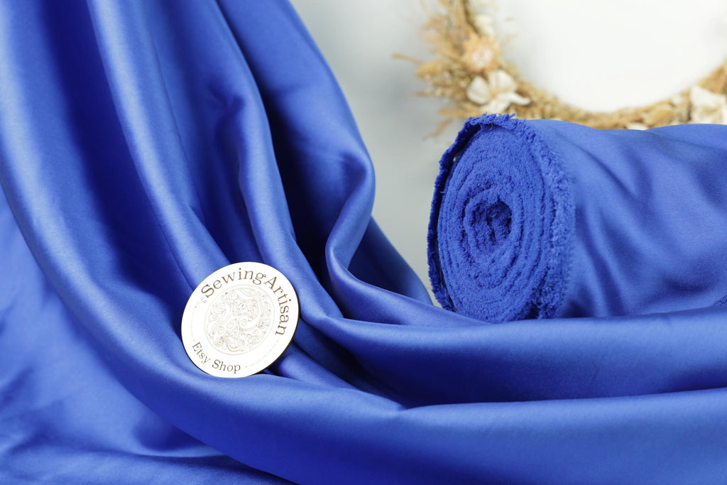 a close-up of a blue satin fabric with a sewing artisan's logo prominently displayed on it.