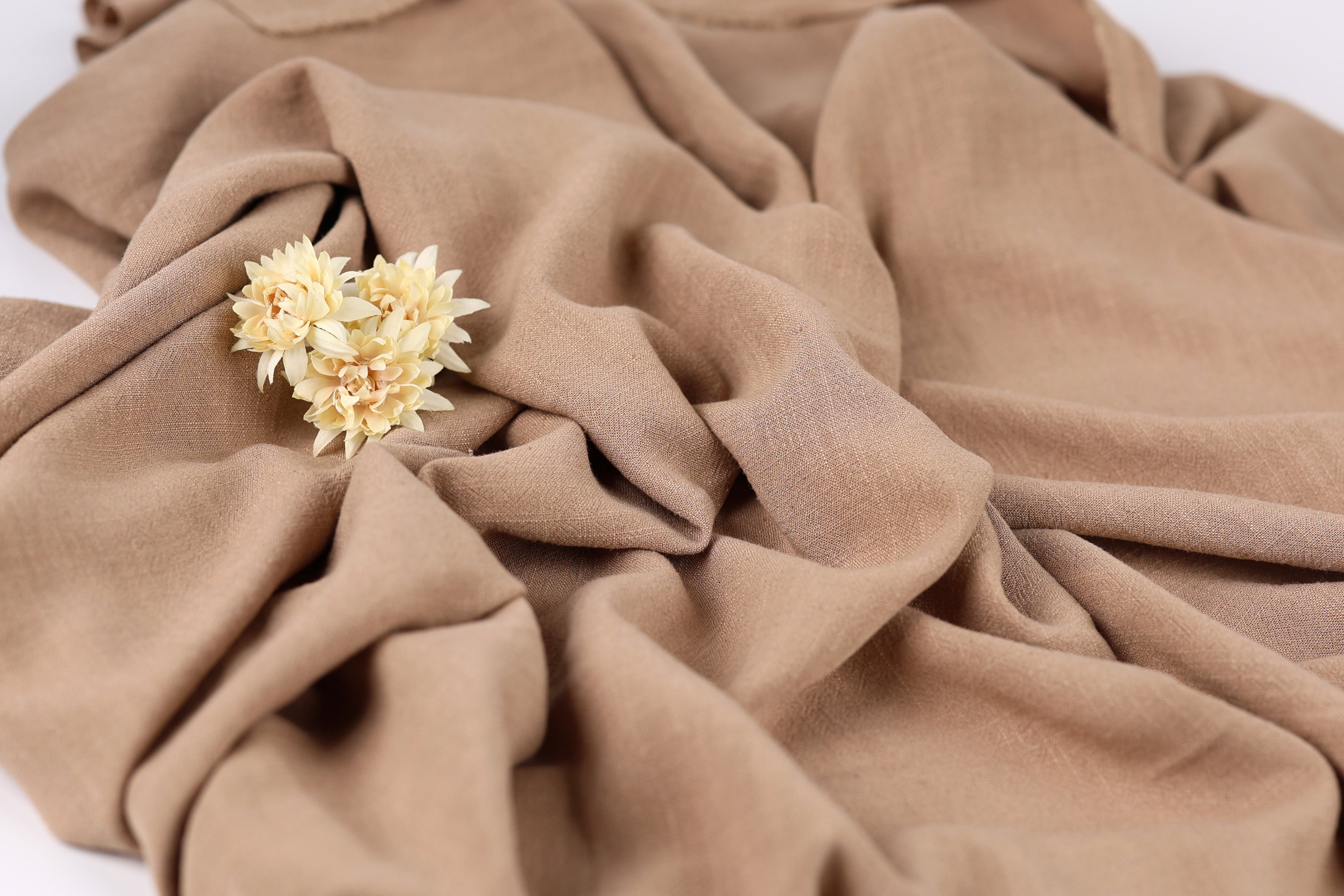 A close-up image of a crumpled beige fabric with a small yellow flower resting on it.