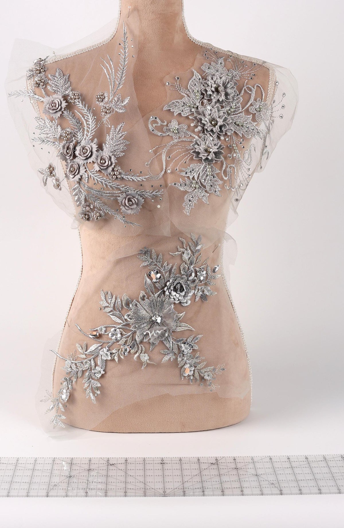 a mannequin with a beige body and a white background. The mannequin is adorned with silver floral and leaf designs, creating a visually striking contrast against the white background.