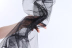 A hand is holding a black, sheer fabric with sparkles on it against a white background.