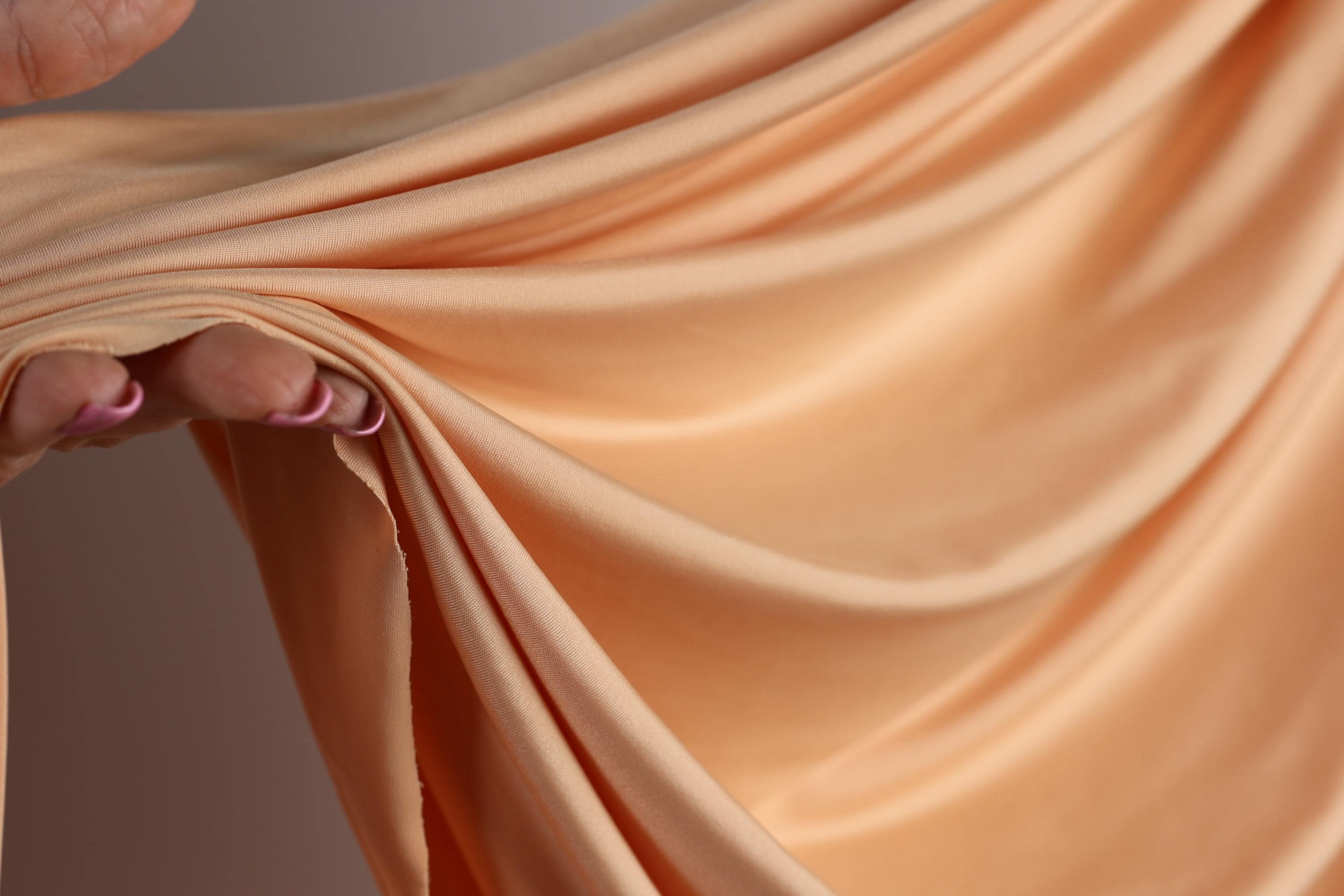 A hand holding a piece of peach-colored fabric, with the fabric being folded and twisted in a way that creates a sense of movement and texture.