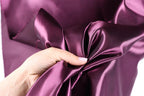 A hand is holding a piece of purple satin fabric, examining its texture and appearance.