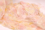 a close-up view of a delicate, sheer fabric with a floral pattern in shades of pink and yellow. The fabric appears to be made of sheer material, giving it a soft and delicate appearance.