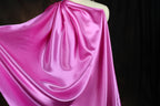 A close-up view of a flowing, shiny pink satin fabric draped over a mannequin.