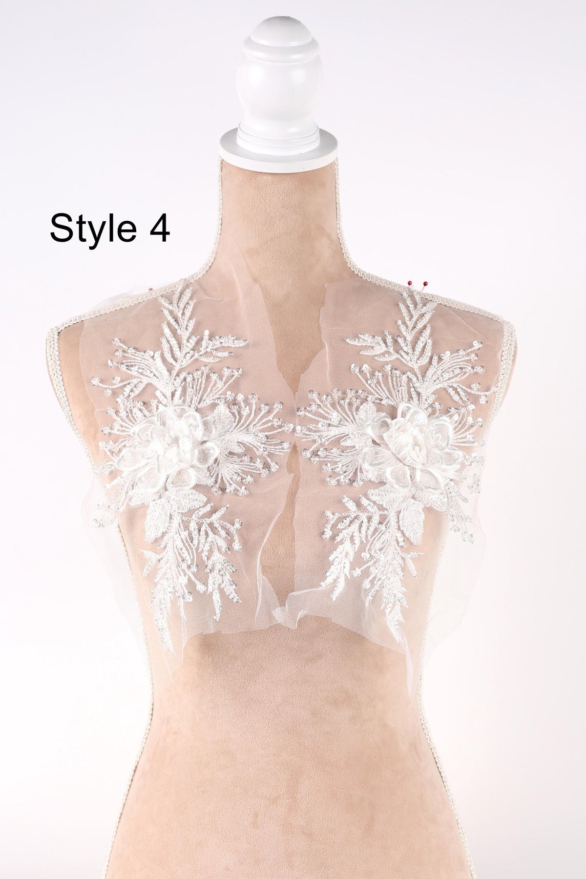 A mannequin wearing a white lace bodice with floral embroidery on the shoulders.