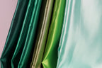 A close-up view of a collection of colorful satin fabric, with a focus on the vibrant green and gold hues.