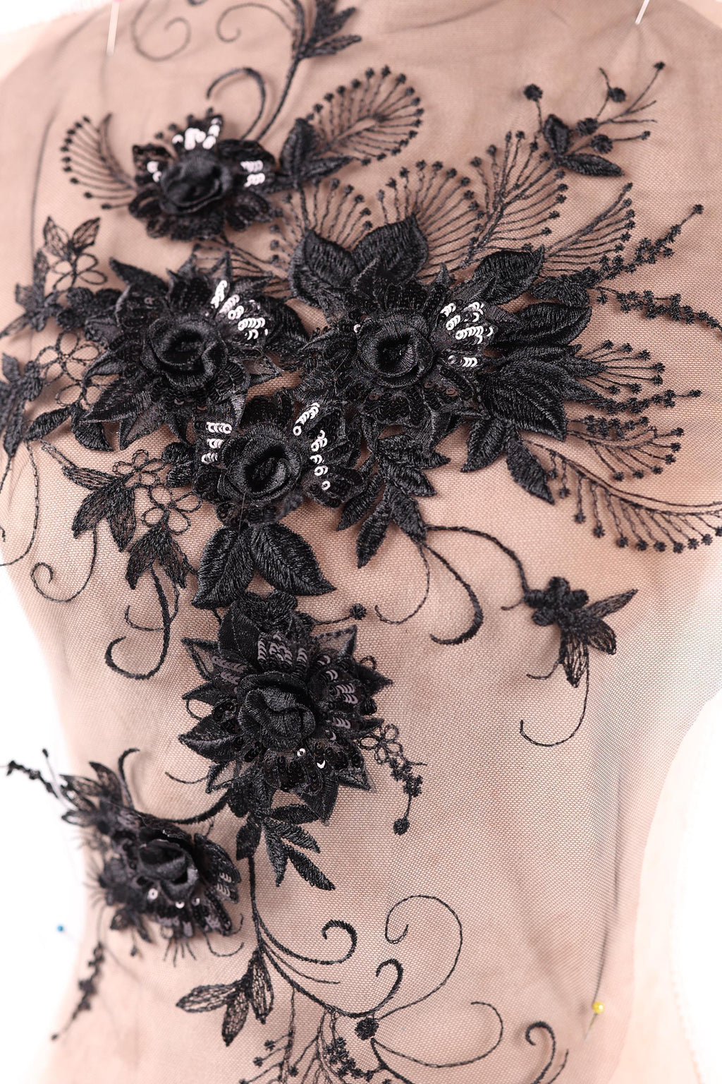 a close-up view of a delicate, intricate black lace design with floral elements. The lace appears to be made of sheer fabric, giving it a delicate and elegant appearance. The design is adorned with black flowers and leaves, which are intricately embroidered or sewn onto the fabric, creating a visually striking and detailed piece of textile art.