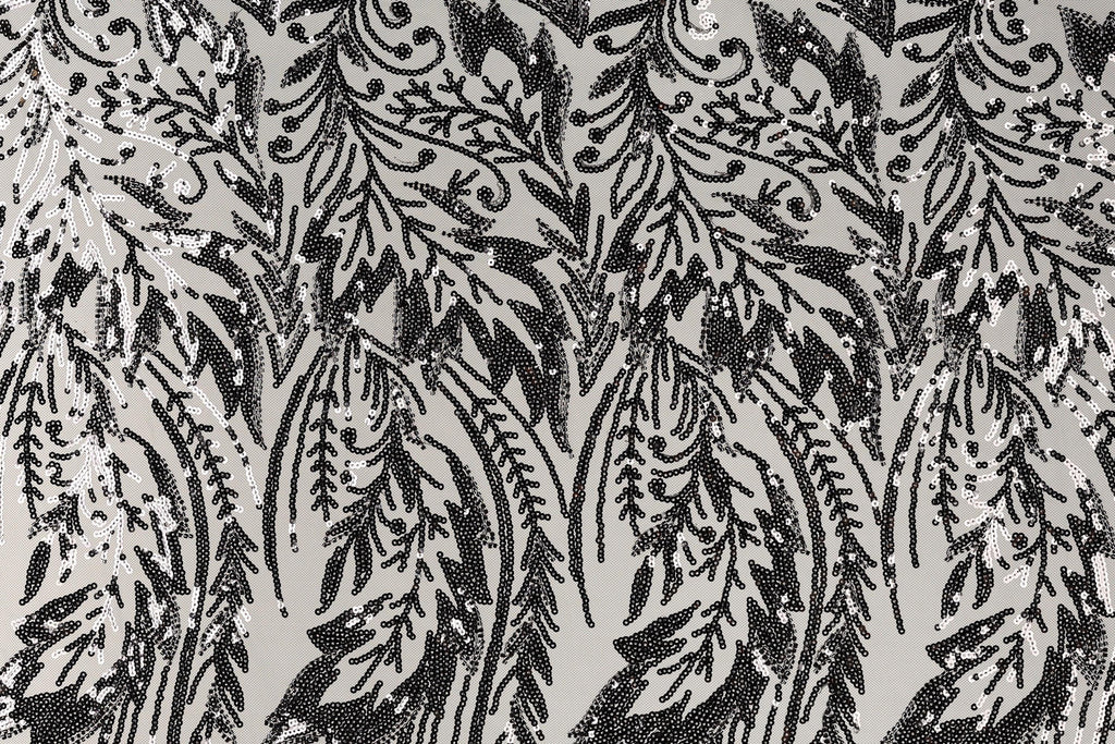 a close-up view of a black and white patterned fabric with a repeating floral or leaf-like design. The pattern consists of numerous small black dots or sequins arranged in a repeating pattern, creating a visually striking and intricate design.