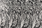 a close-up view of a black and white patterned fabric with a repeating floral or leaf-like design. The pattern consists of numerous small black dots or sequins arranged in a repeating pattern, creating a visually striking and intricate design.