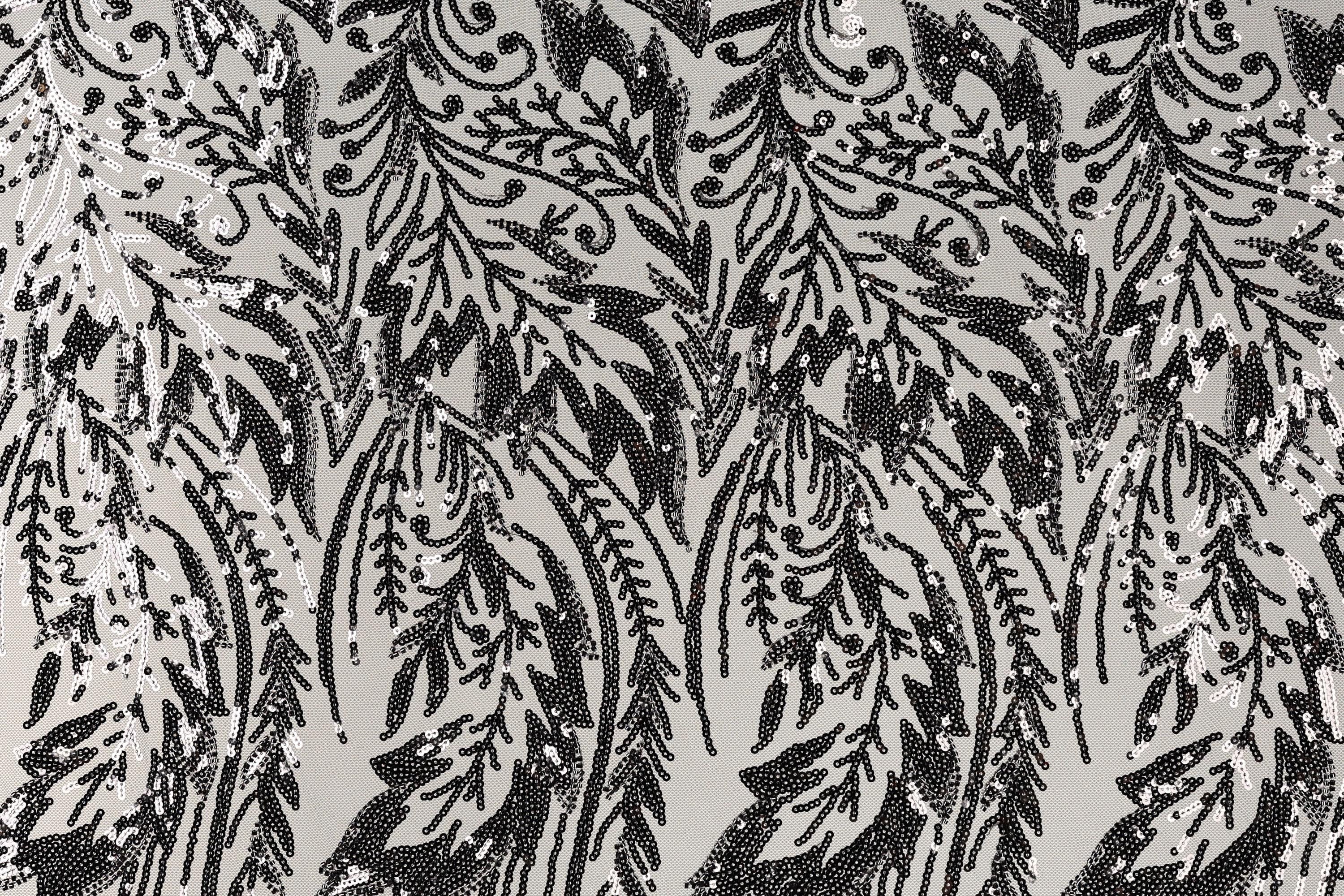 a close-up view of a black and white patterned fabric with a repeating floral or leaf-like design. The pattern consists of numerous small black dots or sequins arranged in a repeating pattern, creating a visually striking and intricate design.
