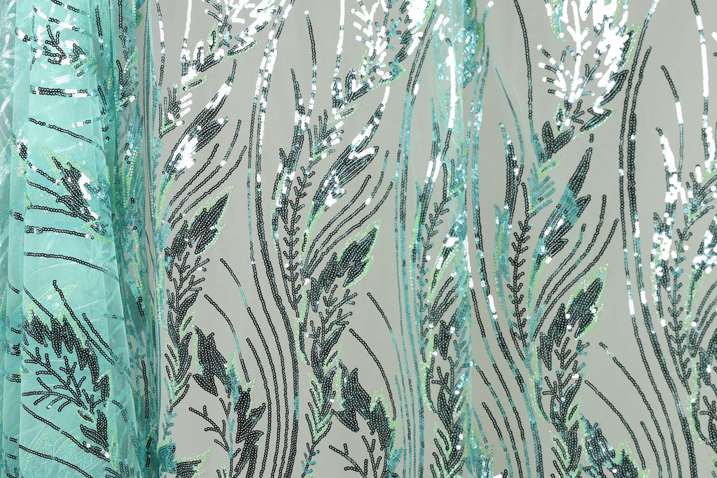 a close-up view of a fabric with a repeating pattern of green and black sequin designs, resembling leaves or grass. The pattern is intricate and detailed, with the sequins arranged in a way that creates a sense of movement and texture. The fabric appears to be a type of textile, possibly used for clothing or home decor.
