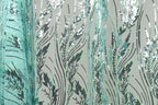 a close-up view of a fabric with a repeating pattern of green and black sequin designs, resembling leaves or grass. The pattern is intricate and detailed, with the sequins arranged in a way that creates a sense of movement and texture. The fabric appears to be a type of textile, possibly used for clothing or home decor.