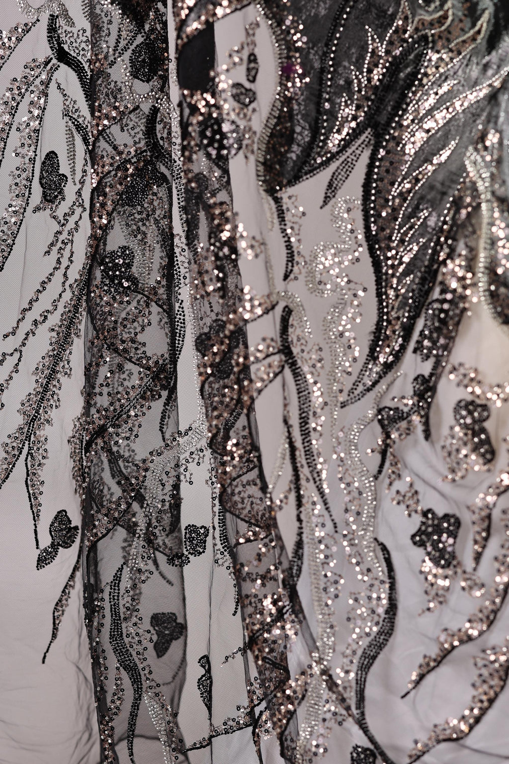The image is a close-up view of a fabric with a black and white pattern, featuring a mix of sequins and lace. The fabric appears to be a sheer material, with a delicate and intricate design.