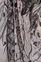 The image is a close-up view of a fabric with a black and white pattern, featuring a mix of sequins and lace. The fabric appears to be a sheer material, with a delicate and intricate design.