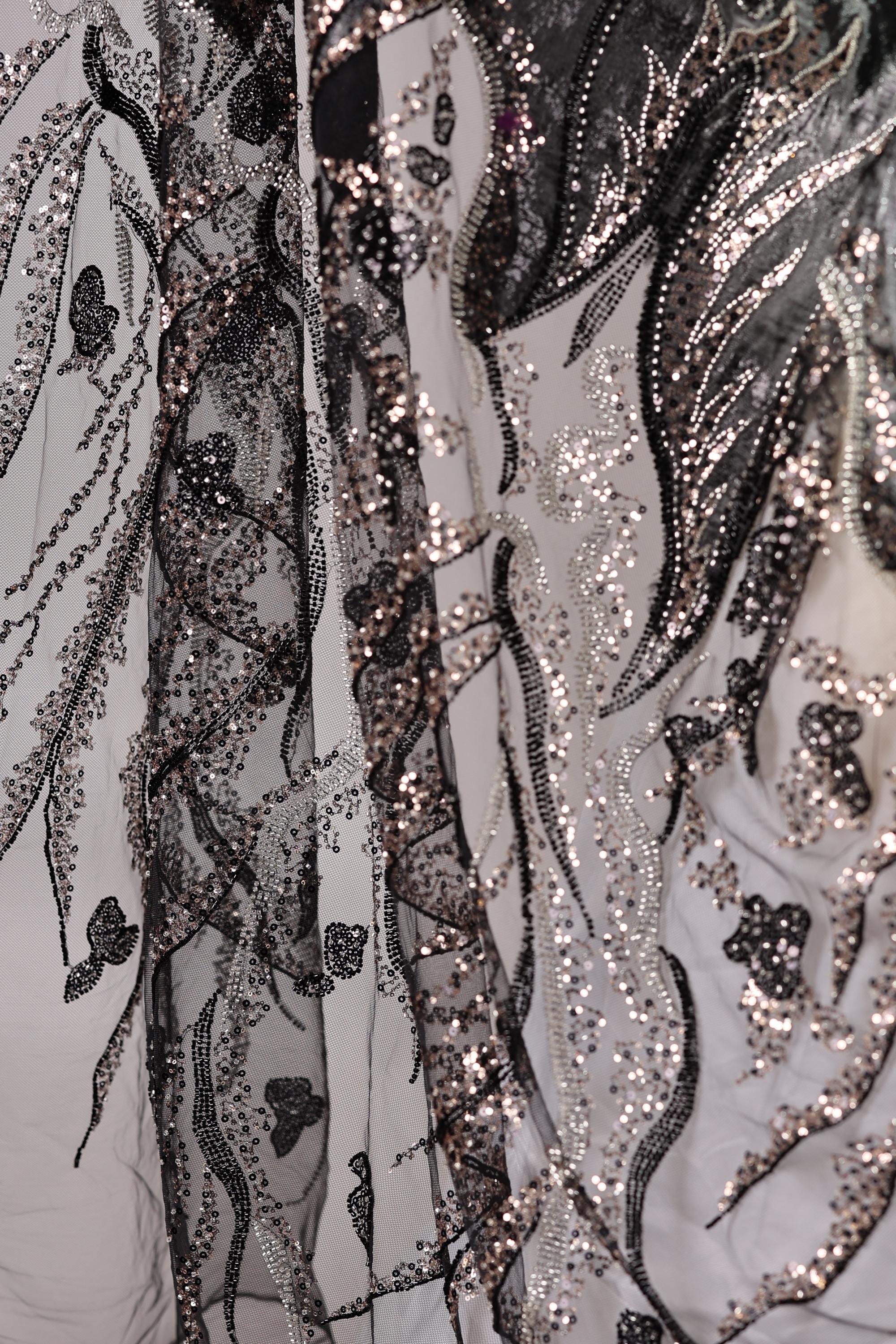 The image is a close-up view of a fabric with a black and white pattern, featuring a mix of sequins and lace. The fabric appears to be a sheer material, with a delicate and intricate design.