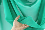 A hand is holding a piece of green fabric, possibly silk, against a blurred background.