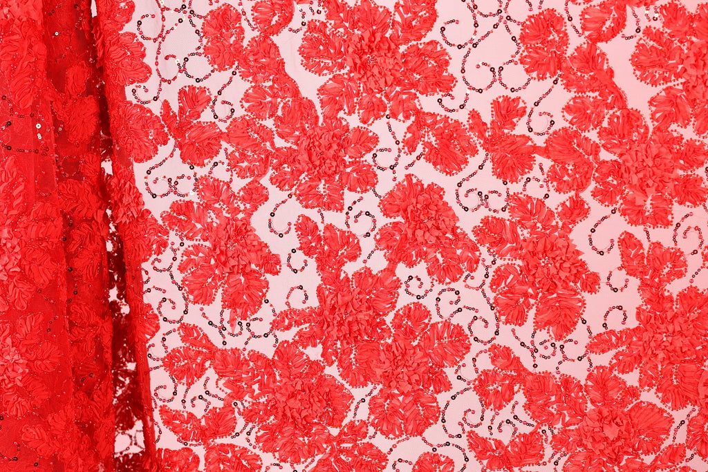 a close-up view of a red fabric with a floral pattern. The fabric appears to be made of a sheer material, with a repeating pattern of red flowers and leaves. The fabric is displayed in a vertical orientation, with the left side of the fabric partially visible.