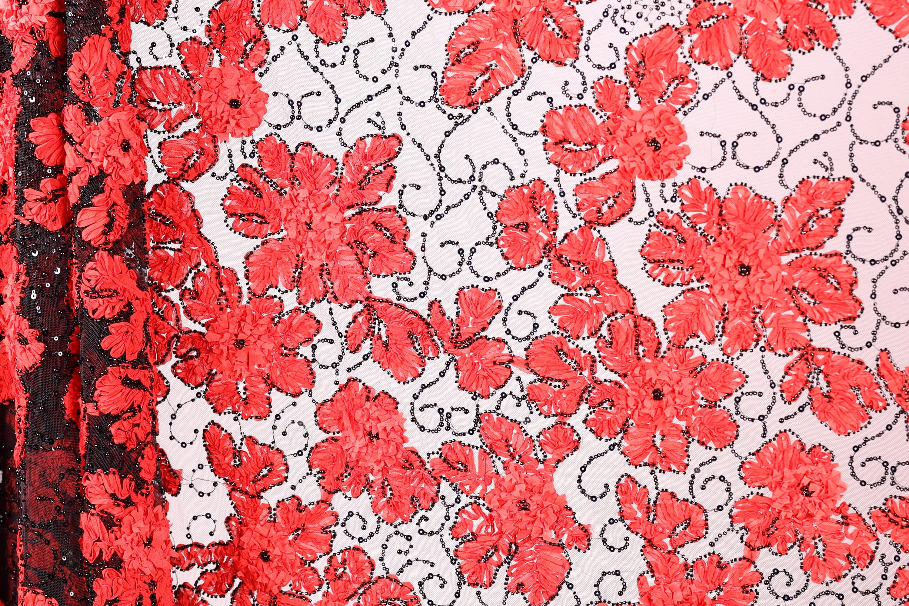 a close-up view of a fabric with a striking red floral pattern. The fabric is adorned with numerous red flowers, each with a black leaf design, creating a visually appealing contrast against the white background. The pattern is intricate and detailed, showcasing the craftsmanship involved in creating this textile.