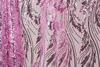 a close-up view of a fabric with a pink and purple sequin pattern. The fabric appears to be a sheer material, with the pink sequins arranged in a zigzag pattern and the purple sequins forming a repeating pattern. The fabric has a textured appearance, with the pink sequins appearing more densely packed than the purple ones. The overall design of the fabric is visually striking and eye-catching.