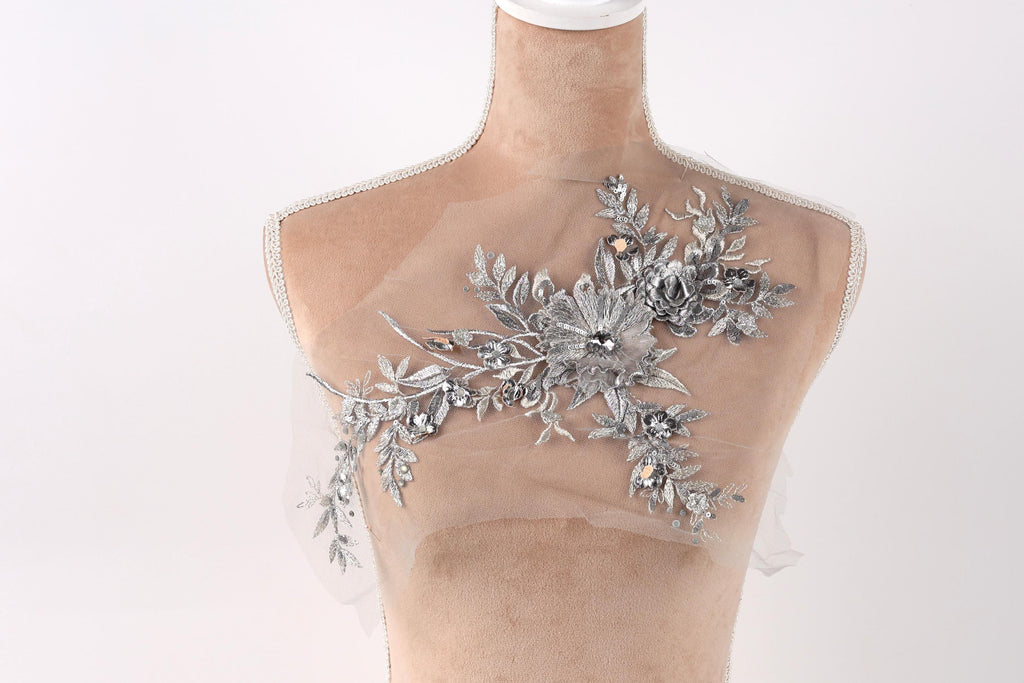 A mannequin with a sheer, transparent fabric draped over its torso, adorned with a floral and leaf-like embellishment.