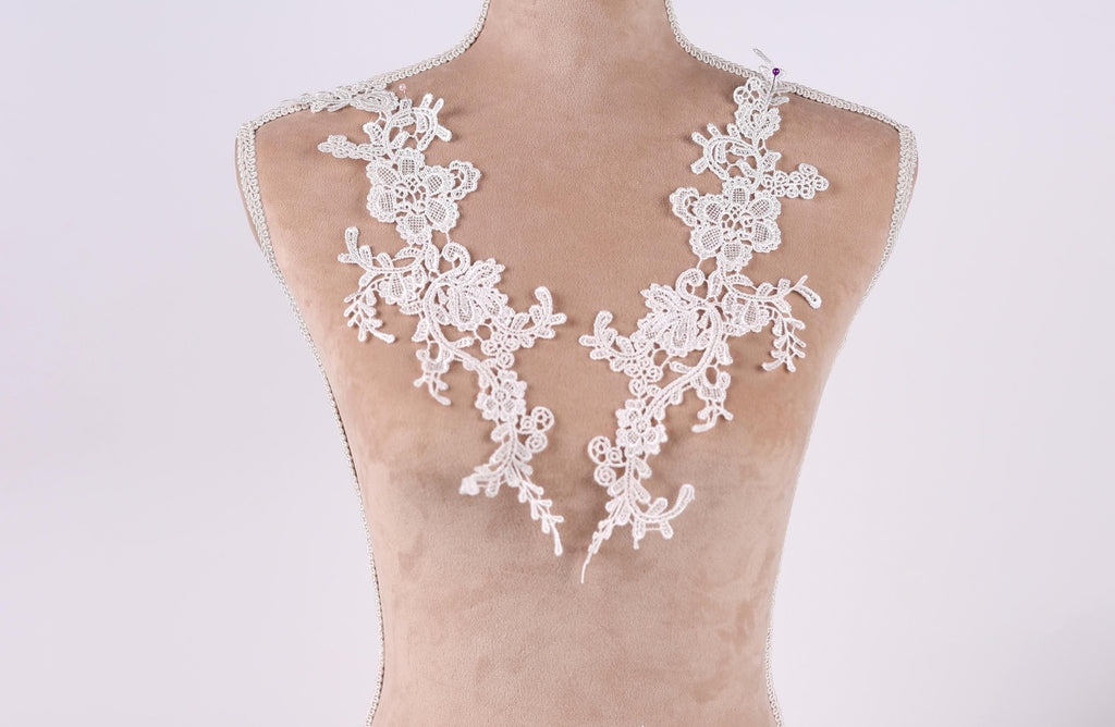 A mannequin wearing a white lace dress with intricate floral patterns.