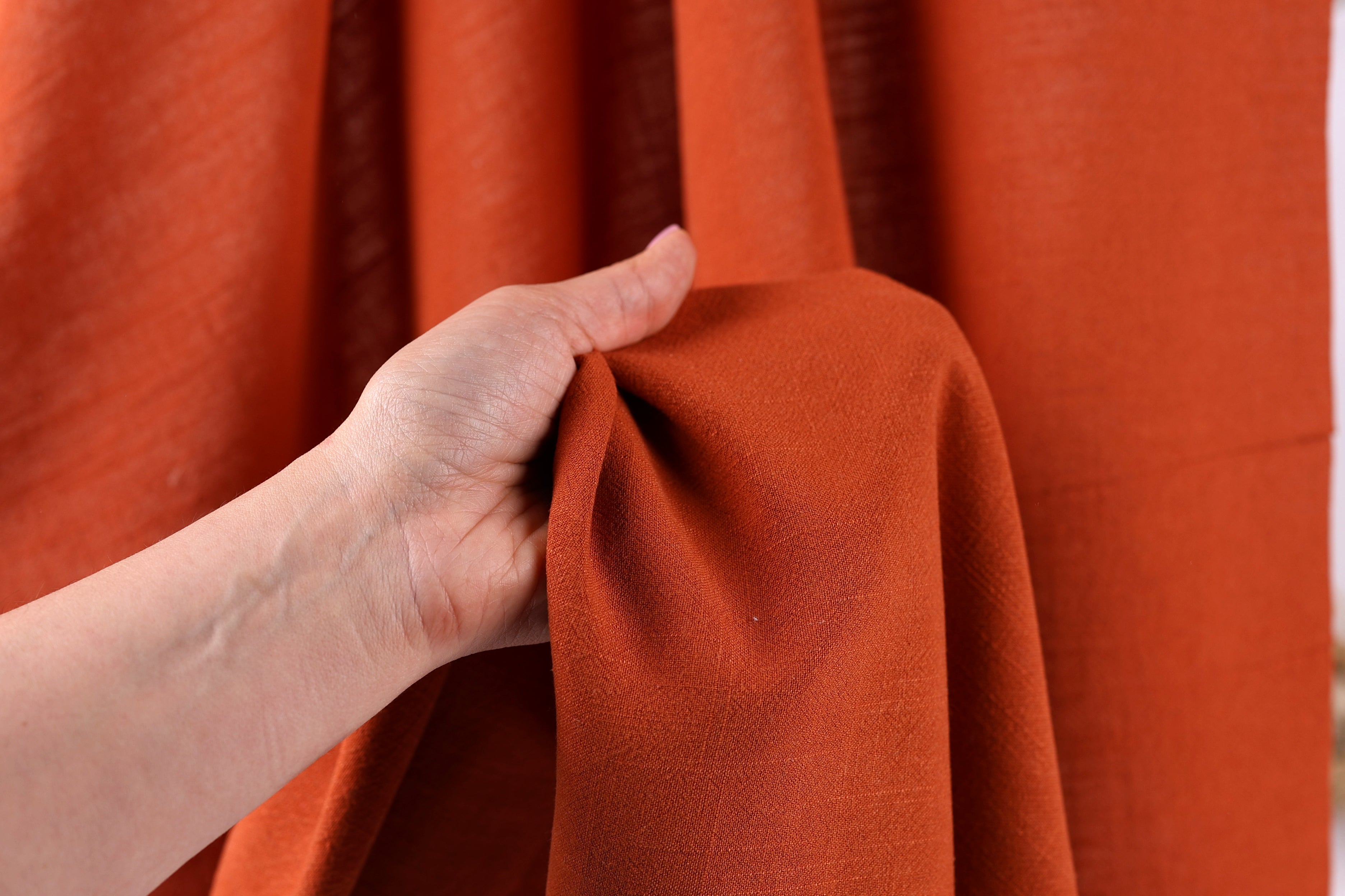 A hand is holding a piece of orange fabric, possibly a curtain or textile, against a red background.