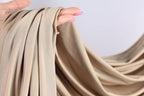 A hand holding a piece of beige fabric, with the fingers of the hand curled around the fabric.