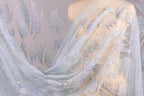 a mannequin wearing a sheer, light blue fabric with a delicate, floral pattern. The fabric appears to be made of sheer material, giving it a delicate and airy appearance. The mannequin is positioned in the center of the image, with the fabric draped over it, showcasing the intricate design and texture of the fabric.