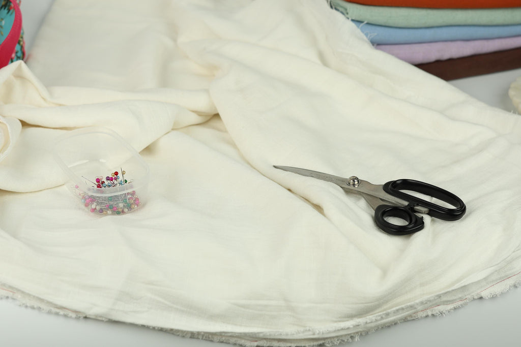 A pair of scissors and a container of colorful beads are placed on a white fabric, suggesting a sewing or crafting project.