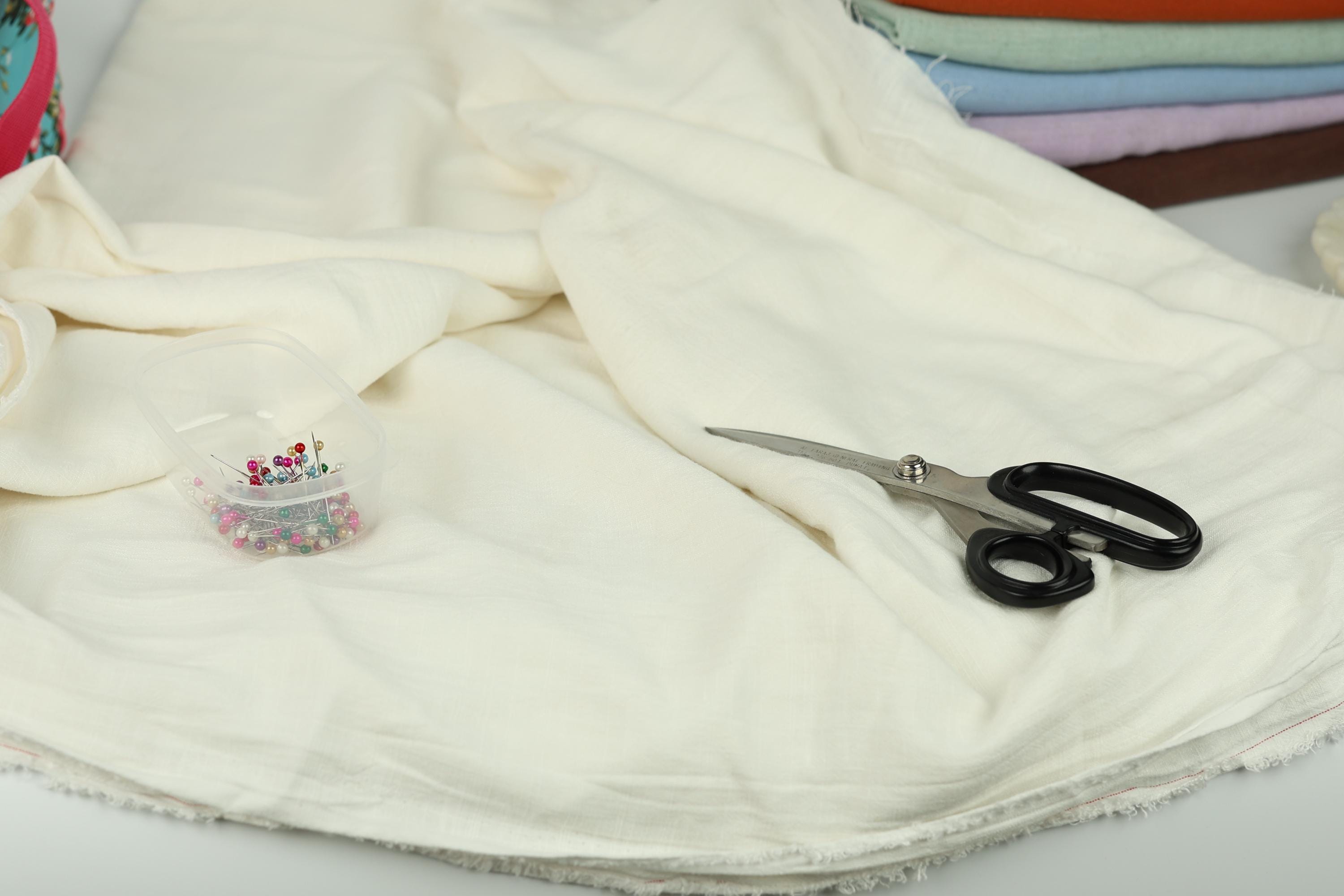 A pair of scissors and a container of colorful beads are placed on a white fabric, suggesting a sewing or crafting project.