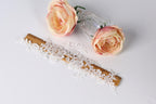 a white lace piece, a wooden ruler, and two pink roses on a white background.
