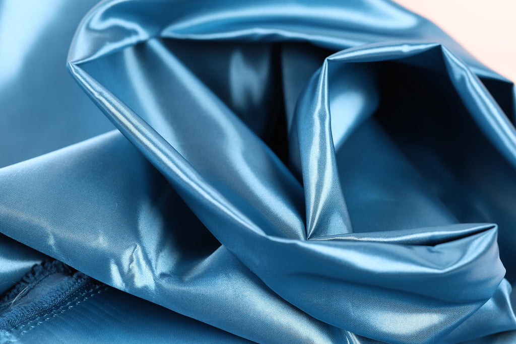 A close-up view of a shiny, blue satin fabric, with a smooth and shiny texture.